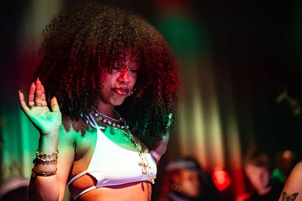 A dancer with a crown of curls under green and red light, 10 October 2026